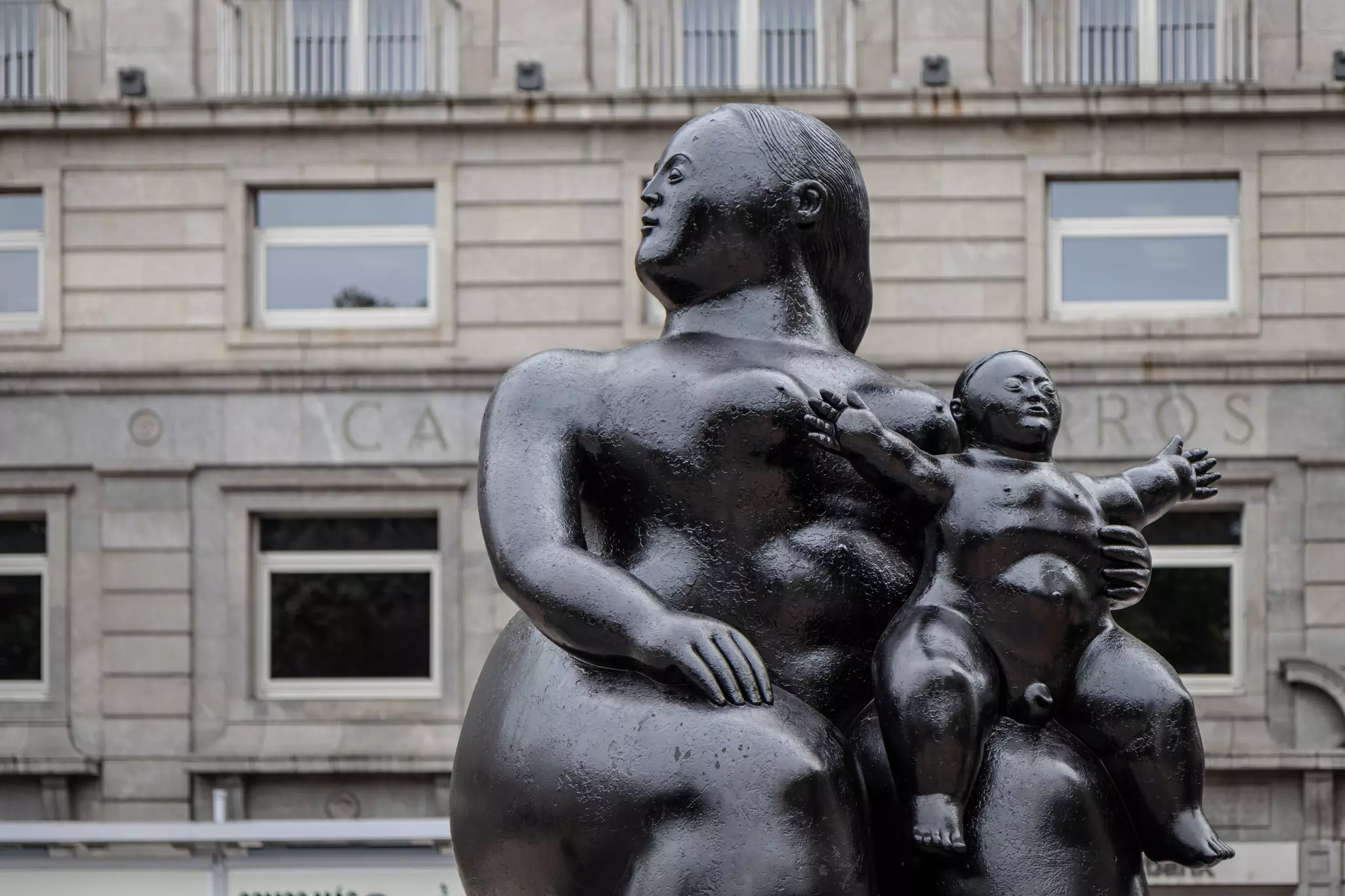 OVIEDO, SPAIN-AUGUST 10, 2021: Close up of La Maternidad sculpture (Sculptor: Fernando Botero) with an historic building in the background.
