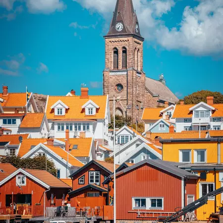 A stone church tower rises above orangish and reddish buildings.