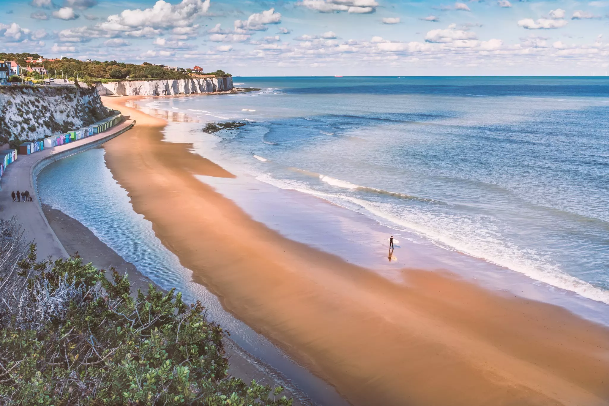 Aerial view of sandy beach with ocean to the right and white cliffs in the distance.