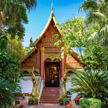 Wat Phra Kaew temple: a small sloping-roofed building, adorned in gold leaf and surrounded by trees and plants.