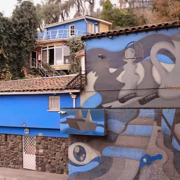 The exterior of a multilevel villa in a city, with one wall painted with a gray-and-blue mural.