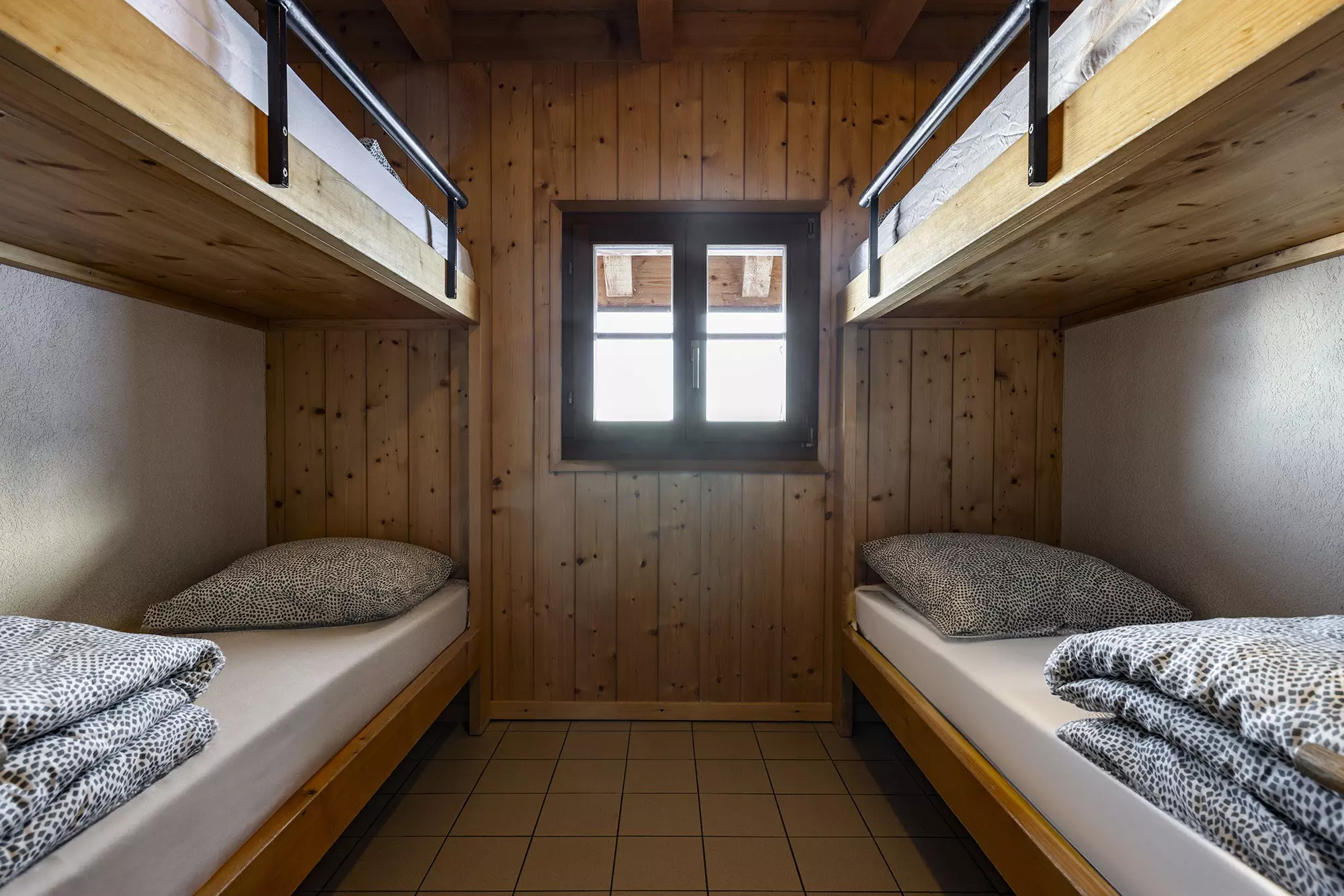 Two sets of bunk beds flush against the walls on opposite sides of a room with a wood-paneled wall that has a window