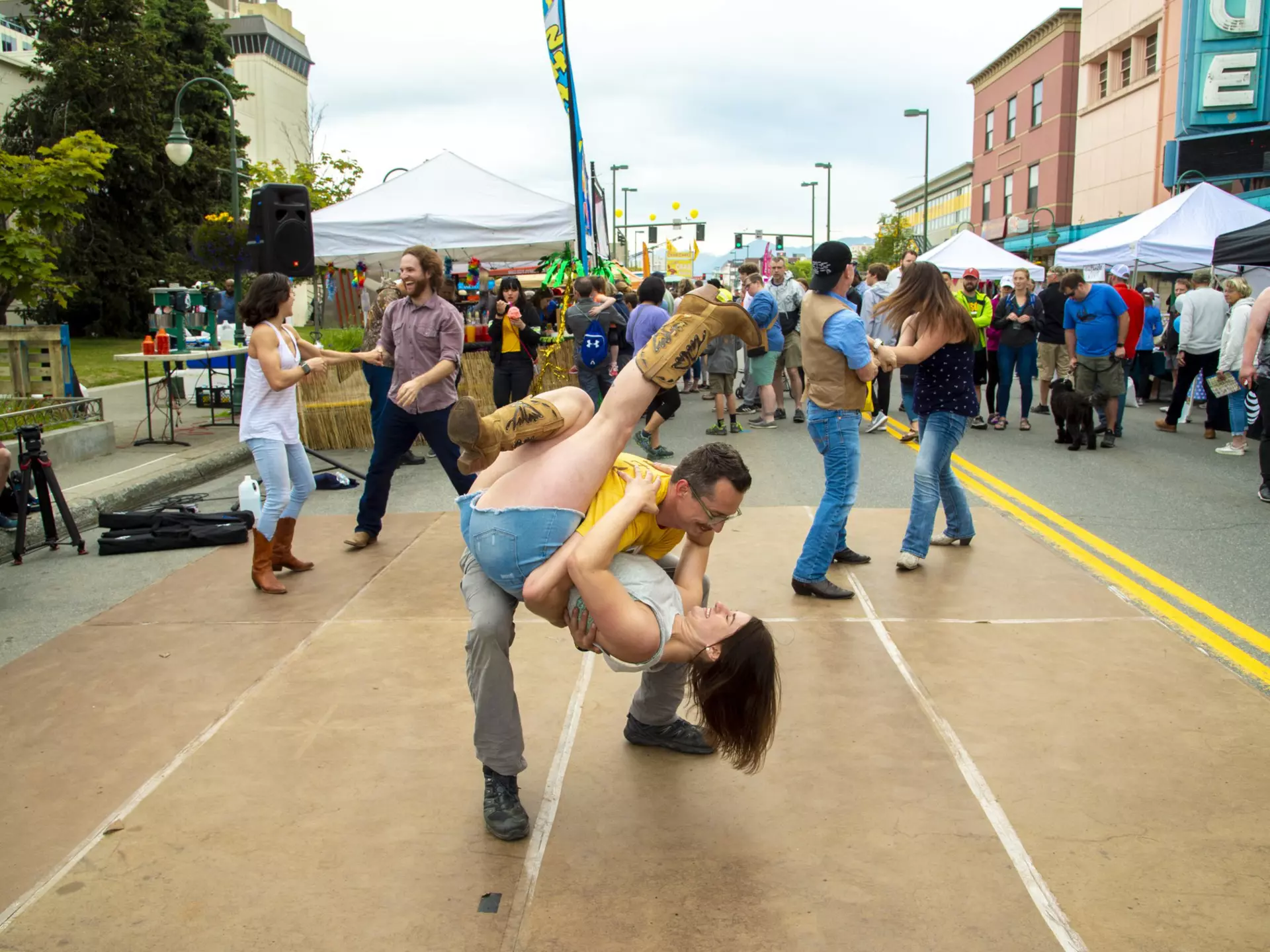 A man picks up a woman as part of a dance routine during a street fair in a city.