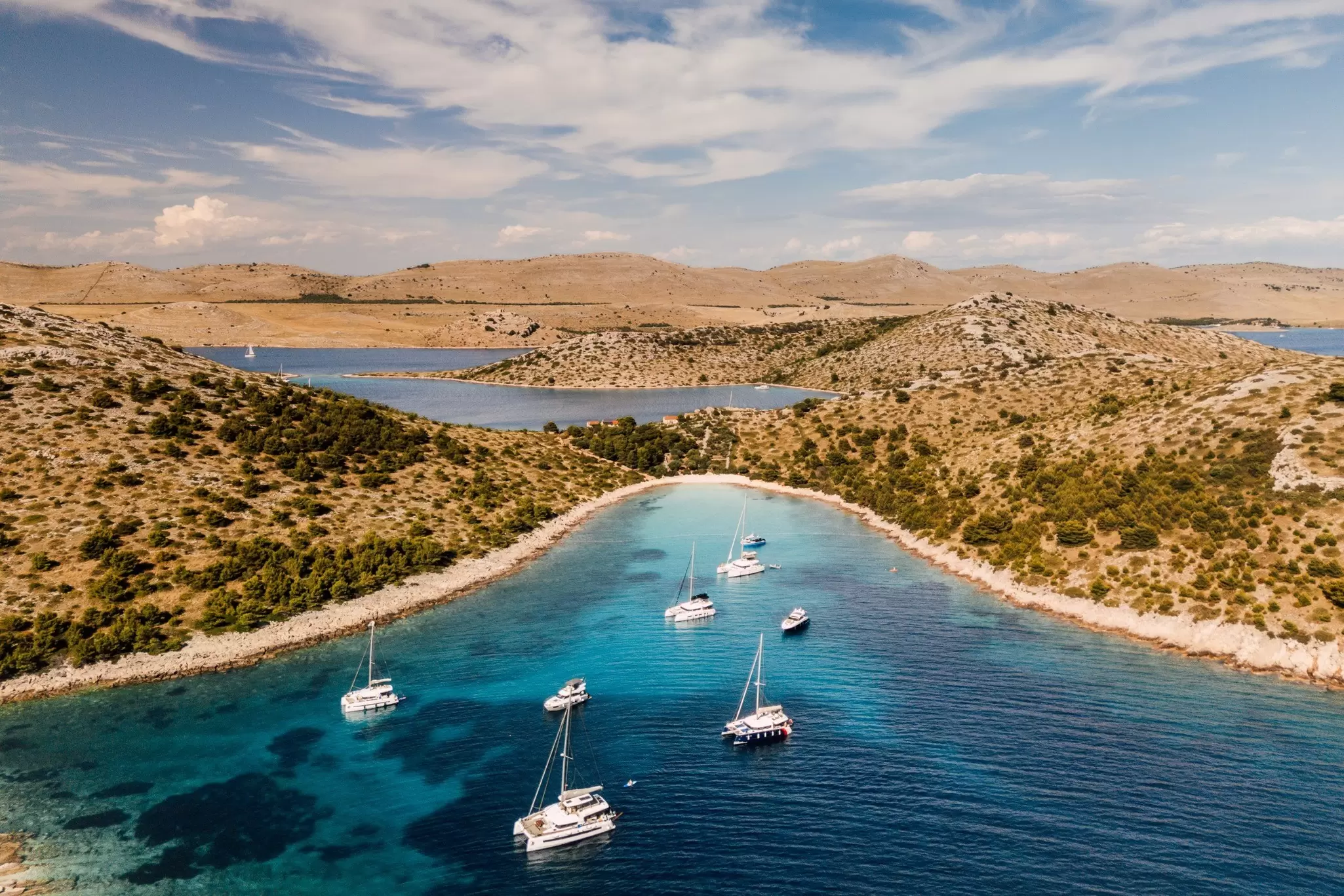 Aerial view of the blue waters along the coastline from Zadar to Šibenik, Croatia with buildings tucked into the landscape under blue sky.