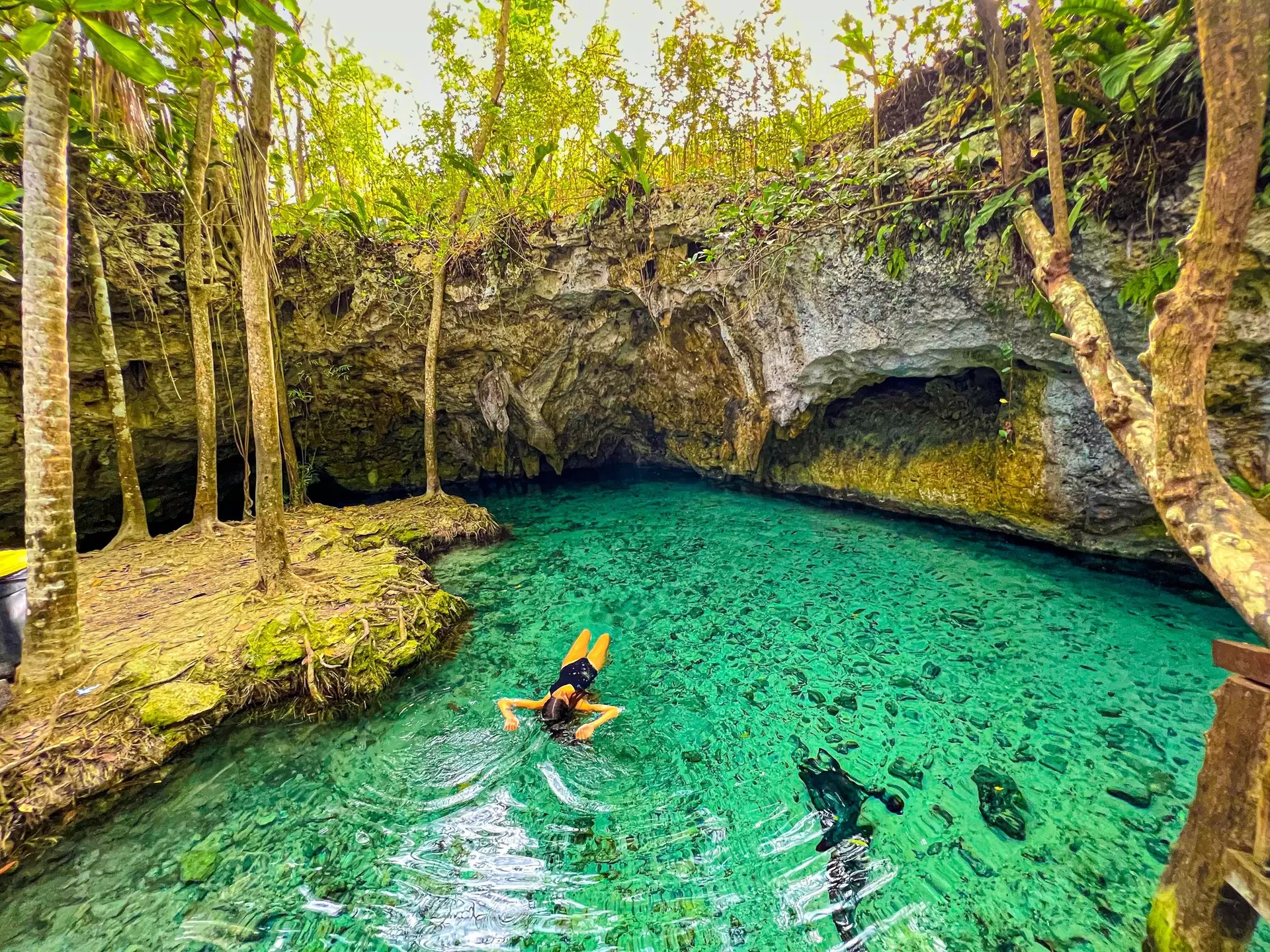 A woman floats on her back in the turquoise waters of a cenote.