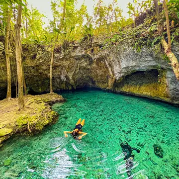 A woman floats on her back in the turquoise waters of a cenote.