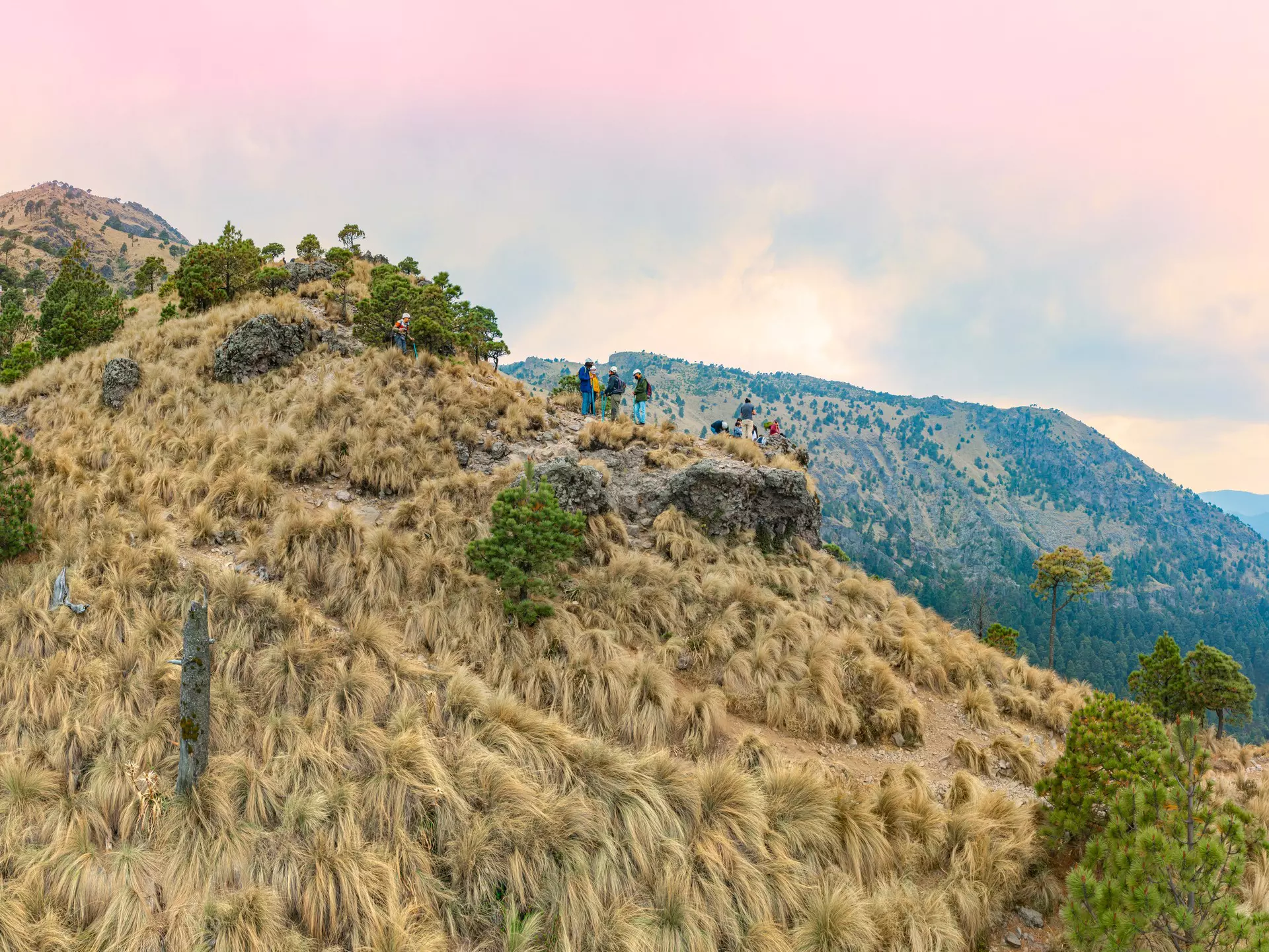 A grass-covered mountain peak with a group of hikers wearing gear and helmets