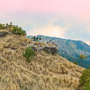 A grass-covered mountain peak with a group of hikers wearing gear and helmets