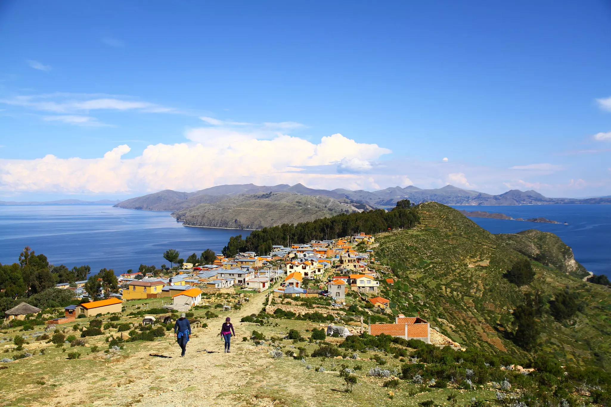 Two people hike up a path near a small settlement on an island in a lake.