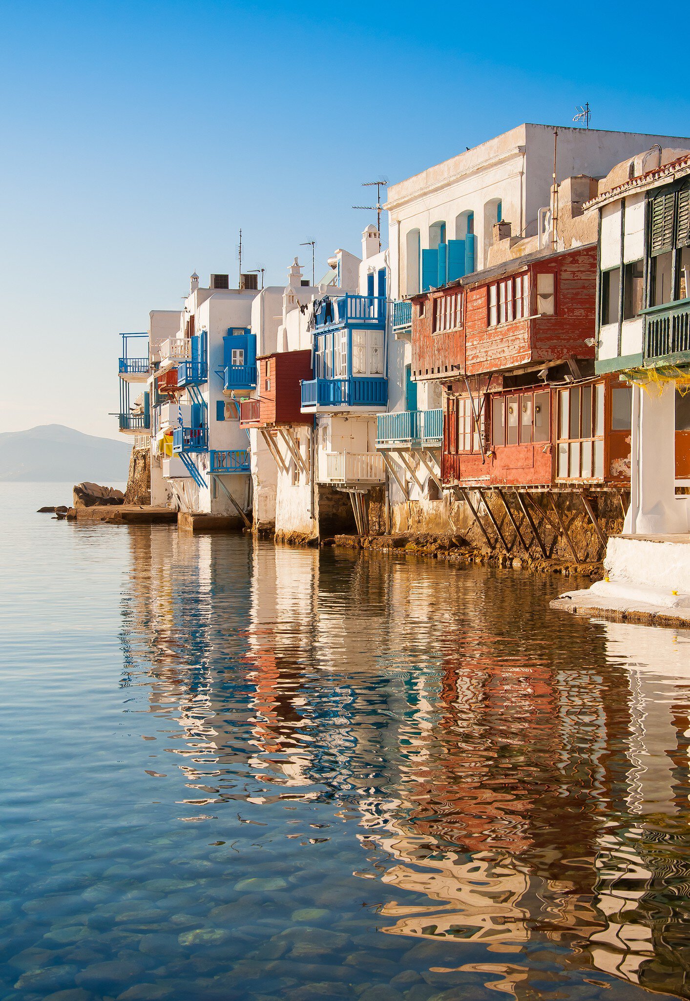View across the water of colorful houses in Little Venice on the island of Mykonos in Greece during sunset.