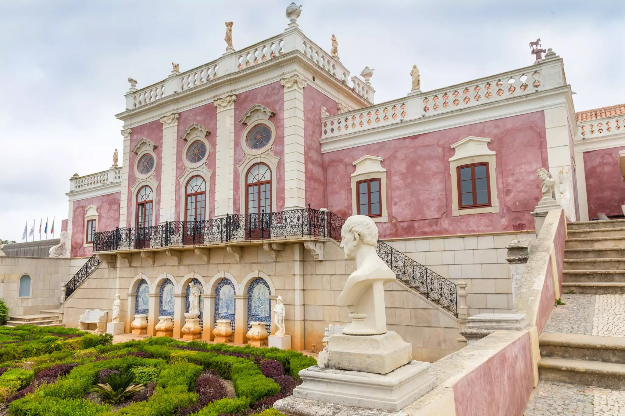 A pink and white ornate building with manicured low bushes in front