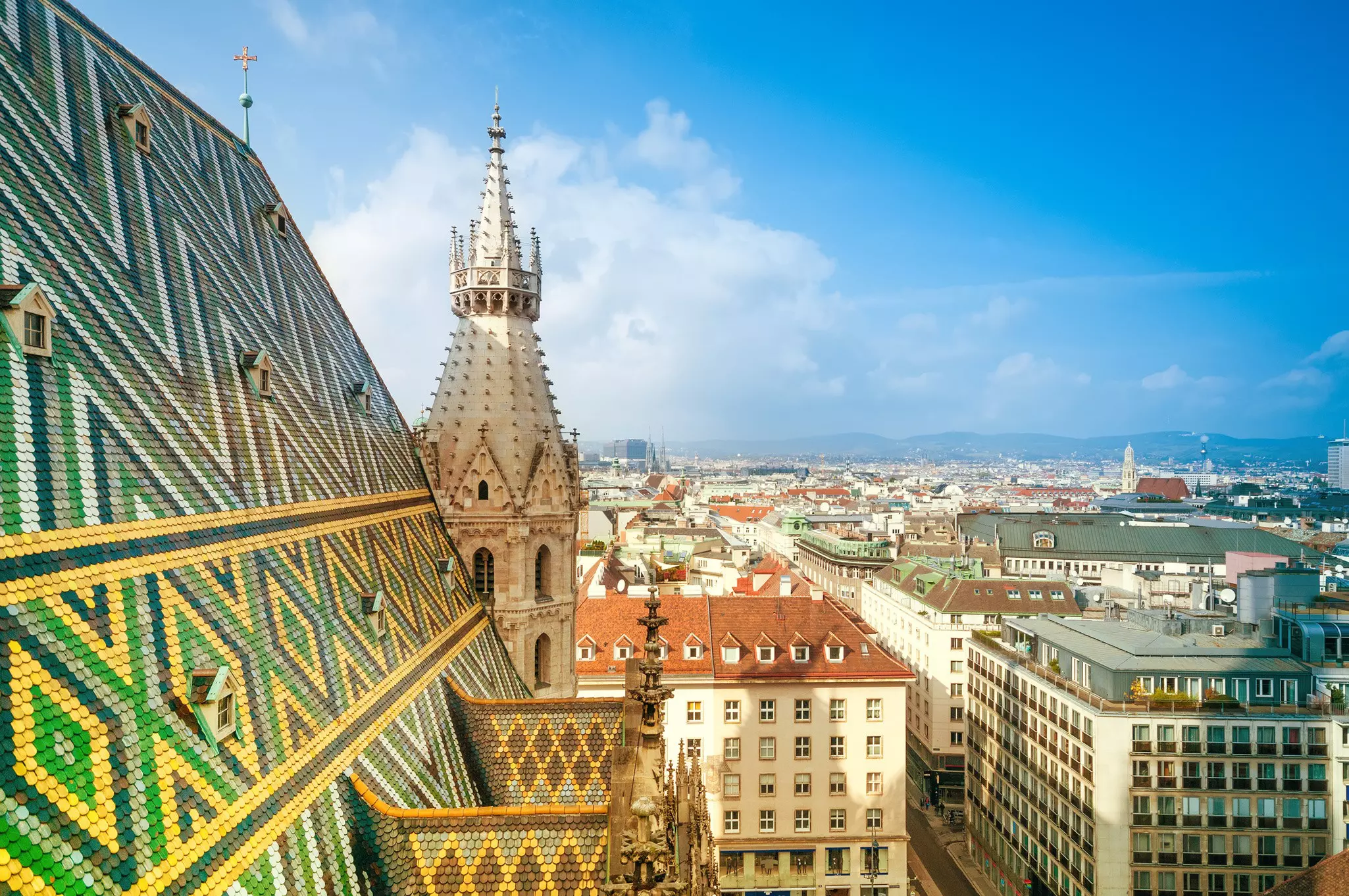 A view down over city streets from a patterned tiled roof of a vast cathedral building