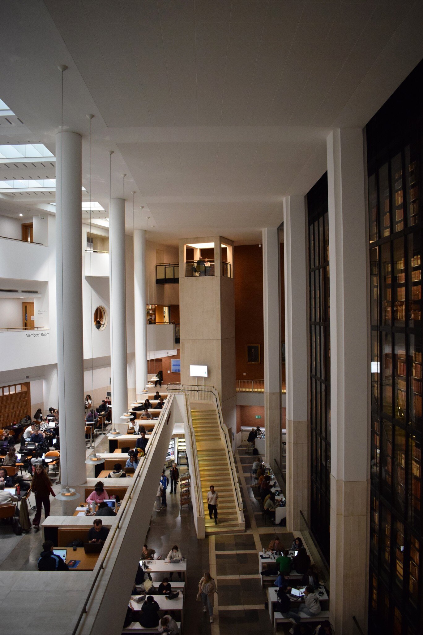 Aerial view inside the British Library, showing people studying around the atrium space next to the King’s Library—the famous glass-enclosed book tower, in London, UK.
