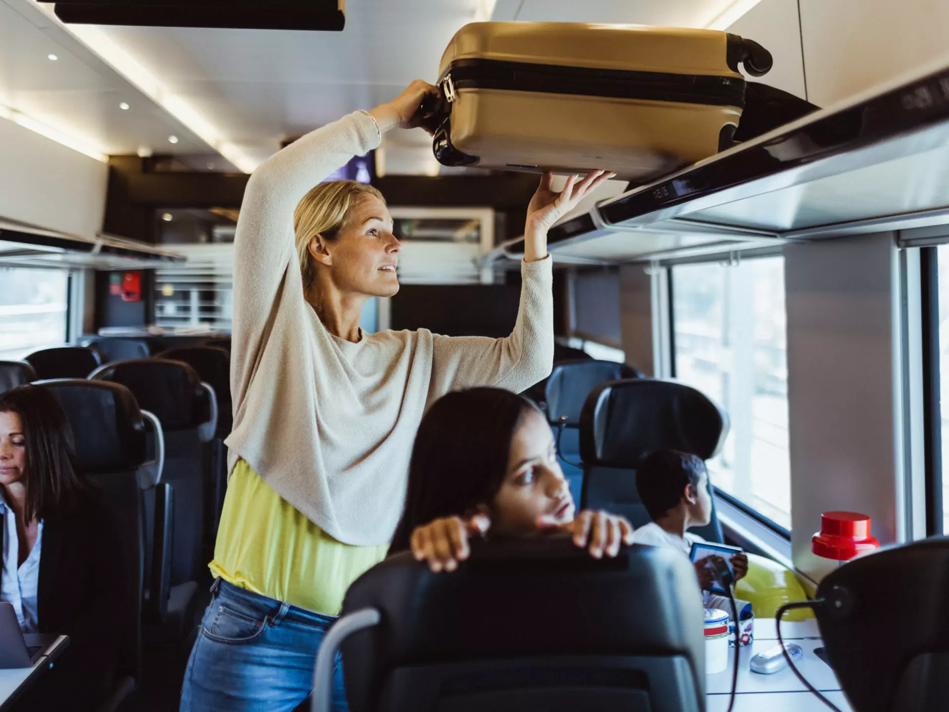Woman arranging luggage on shelf while traveling with children in train