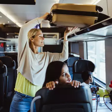 Woman arranging luggage on shelf while traveling with children in train