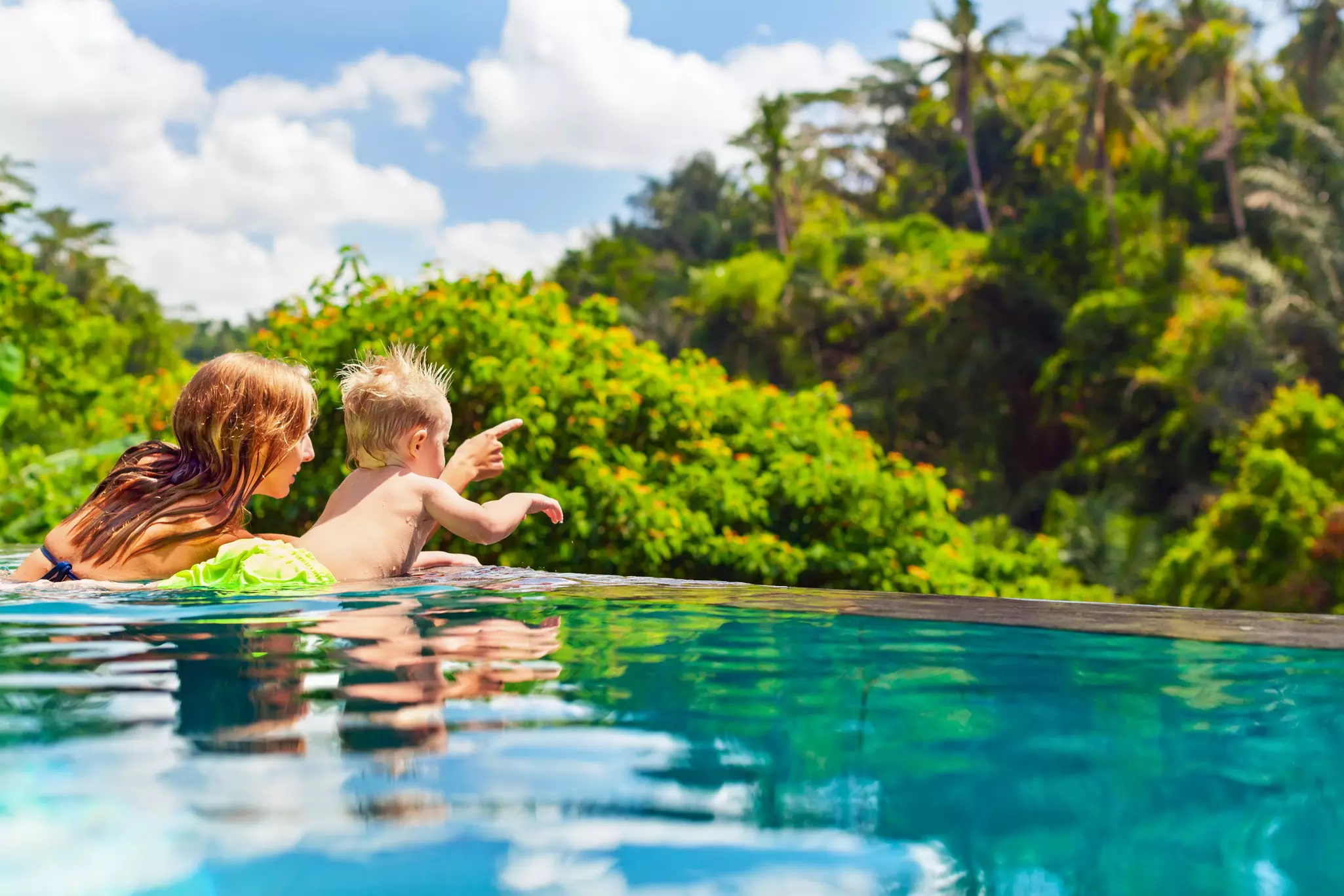 Mother pointing out something to her son in an infinity swimming pool during summer.