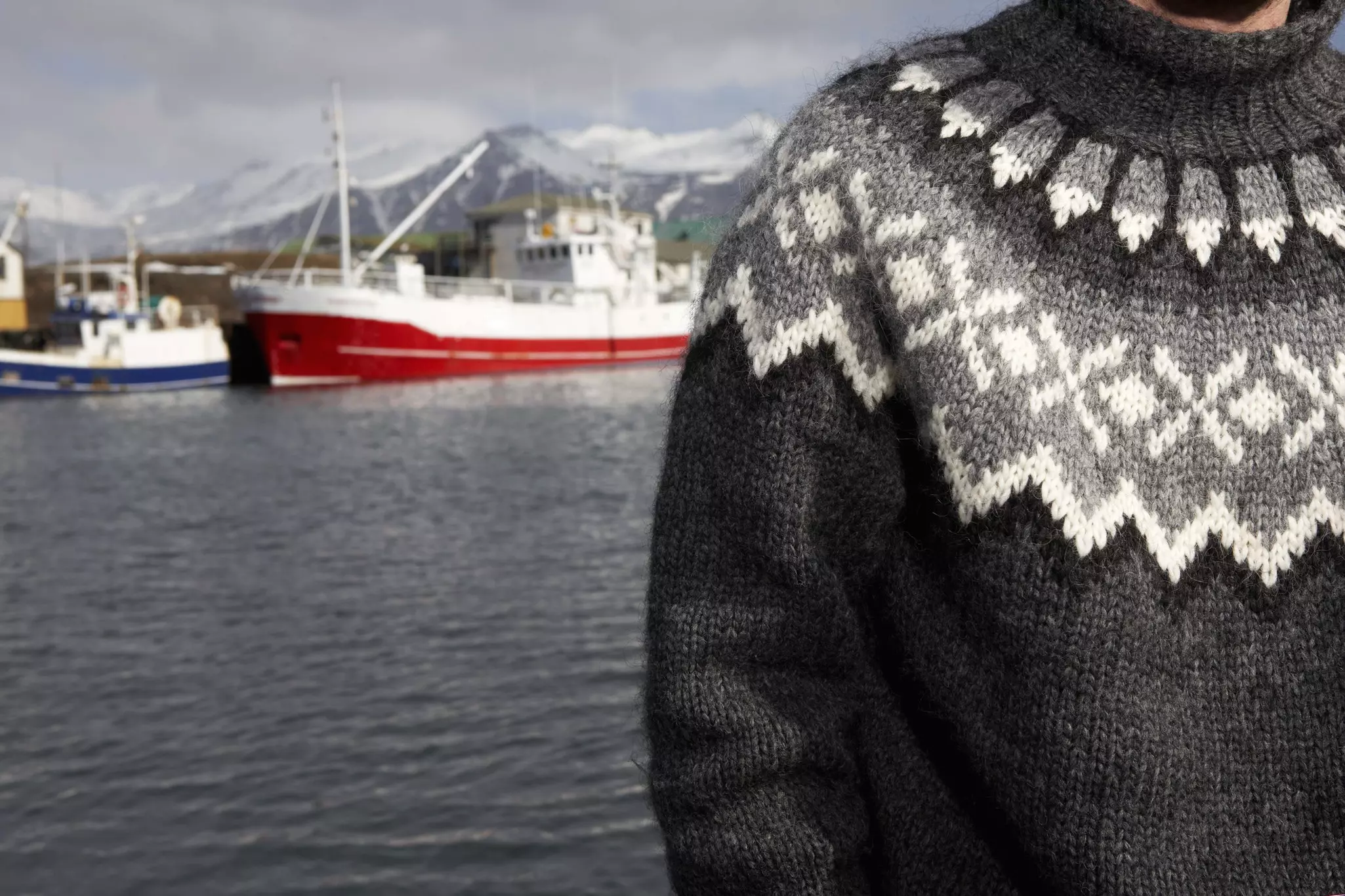 A person wearing a wool sweater near a boat on the water.