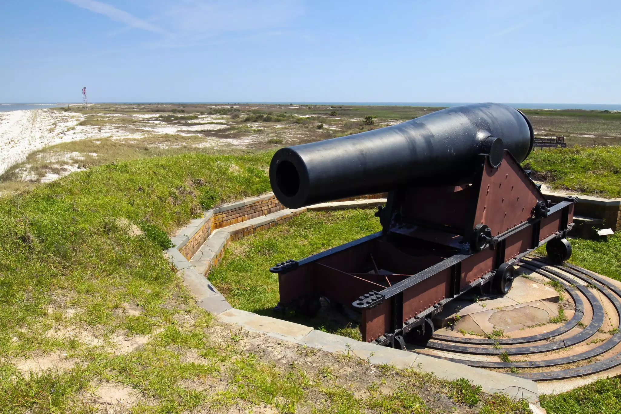 A historic iron cannon sits atop dunes on a barrier island.