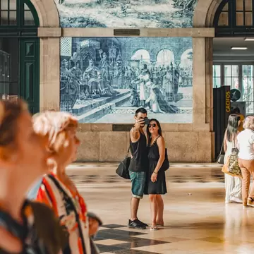 A couple taking a selfie in front of a traditional and typical blue tile art in São Bento train station in Porto, Portugal.