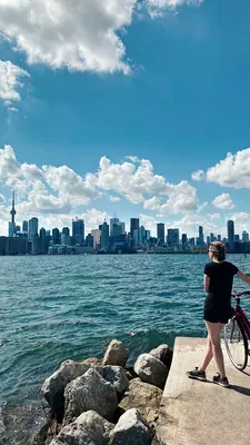 Young woman with bicycle looking out over the ocean towards a large city skyline