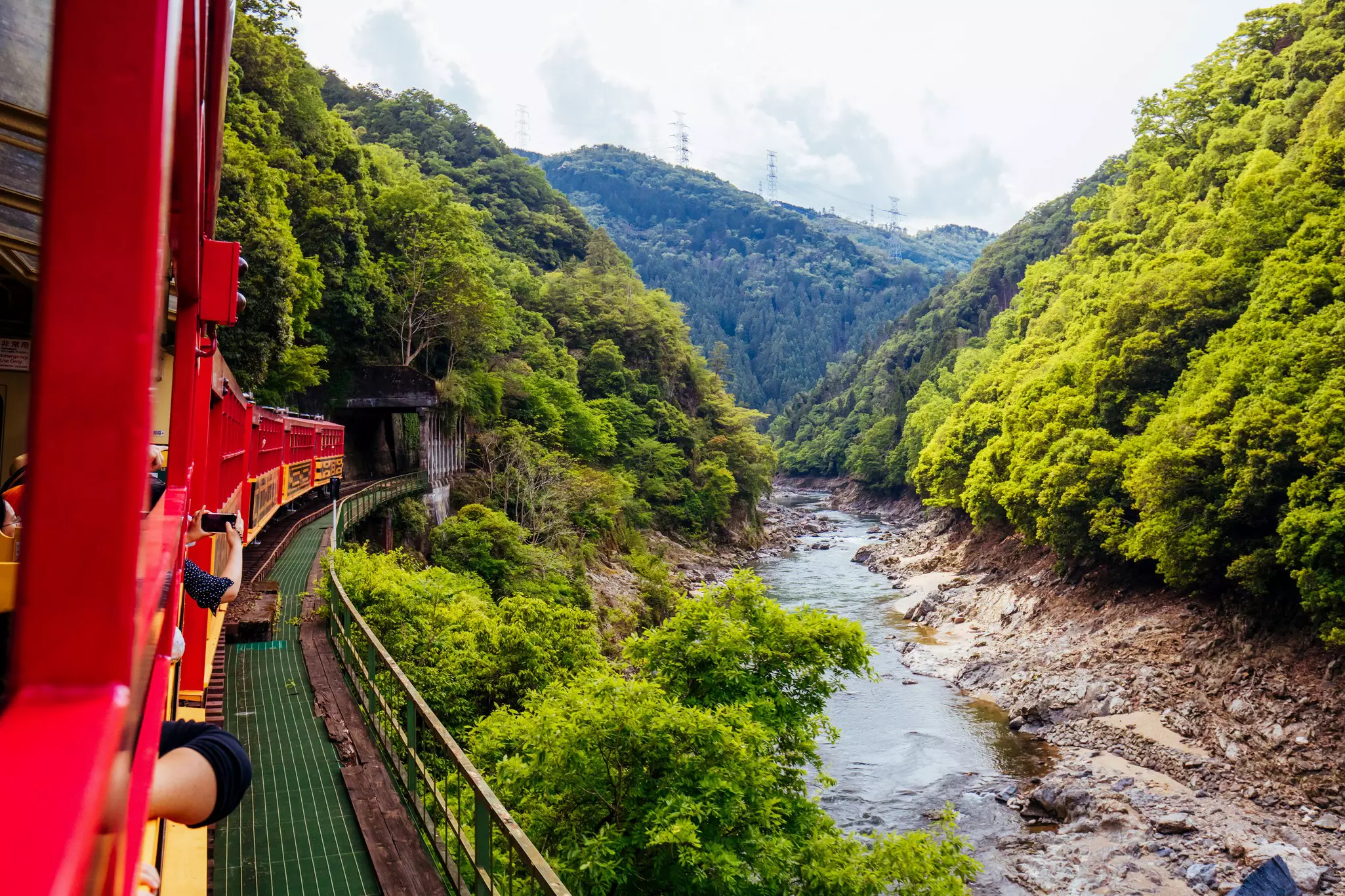 An open-sided tourist train runs along a track at the edge of a gorge beside a river