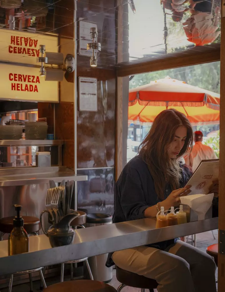 A woman reading the menu while seated near the window at Tacos del Valle in the Roma Norte neighborhood