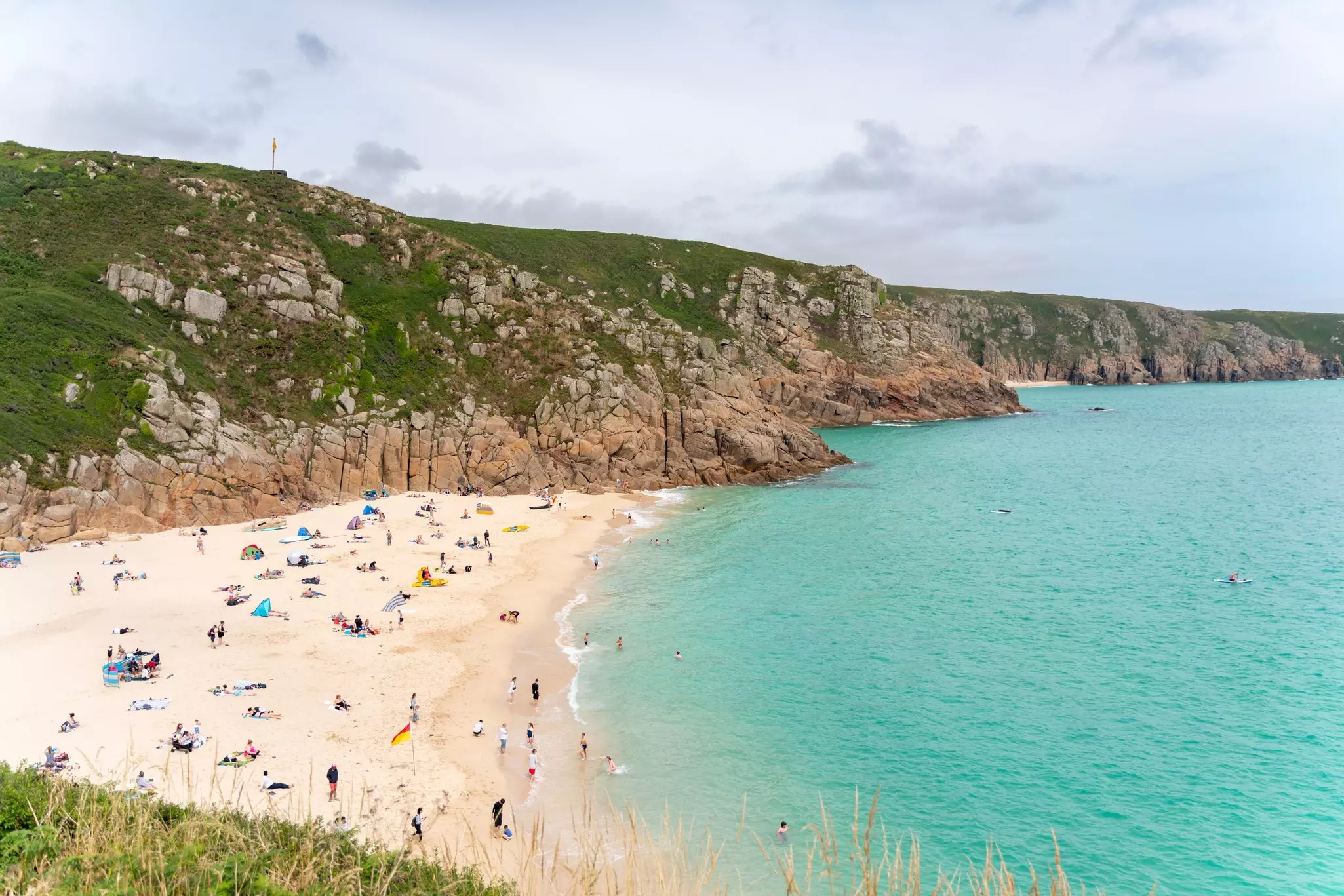 People on a white-sand beach sheltered by cliffs as turquoise water laps at the shore.