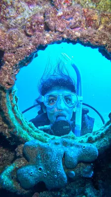 A woman in a scuba mask underwater peers through a porthole.