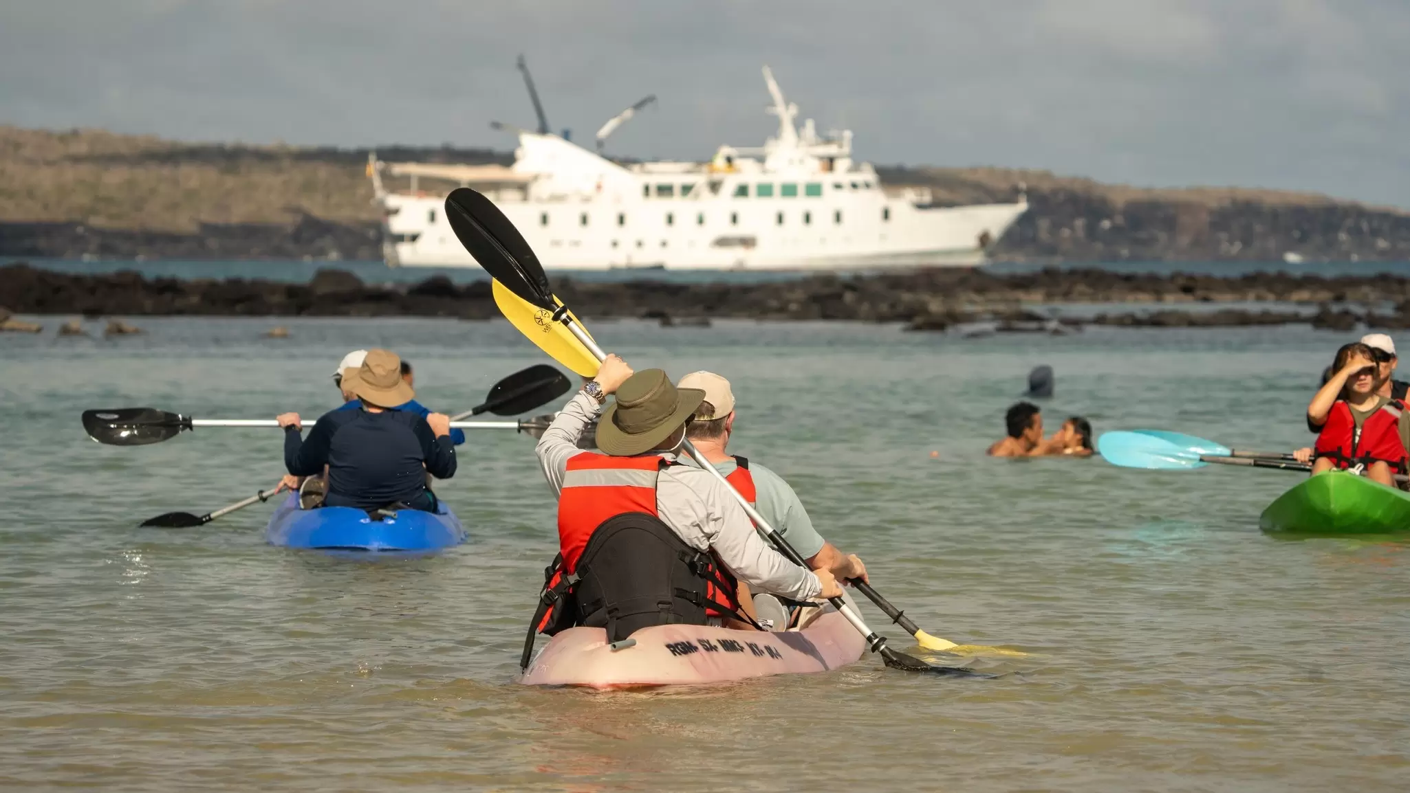 Several people kayak and swim in a lagoon, their cruise ship visible in the distance, Santa Cruz Island, the Galápagos Islands