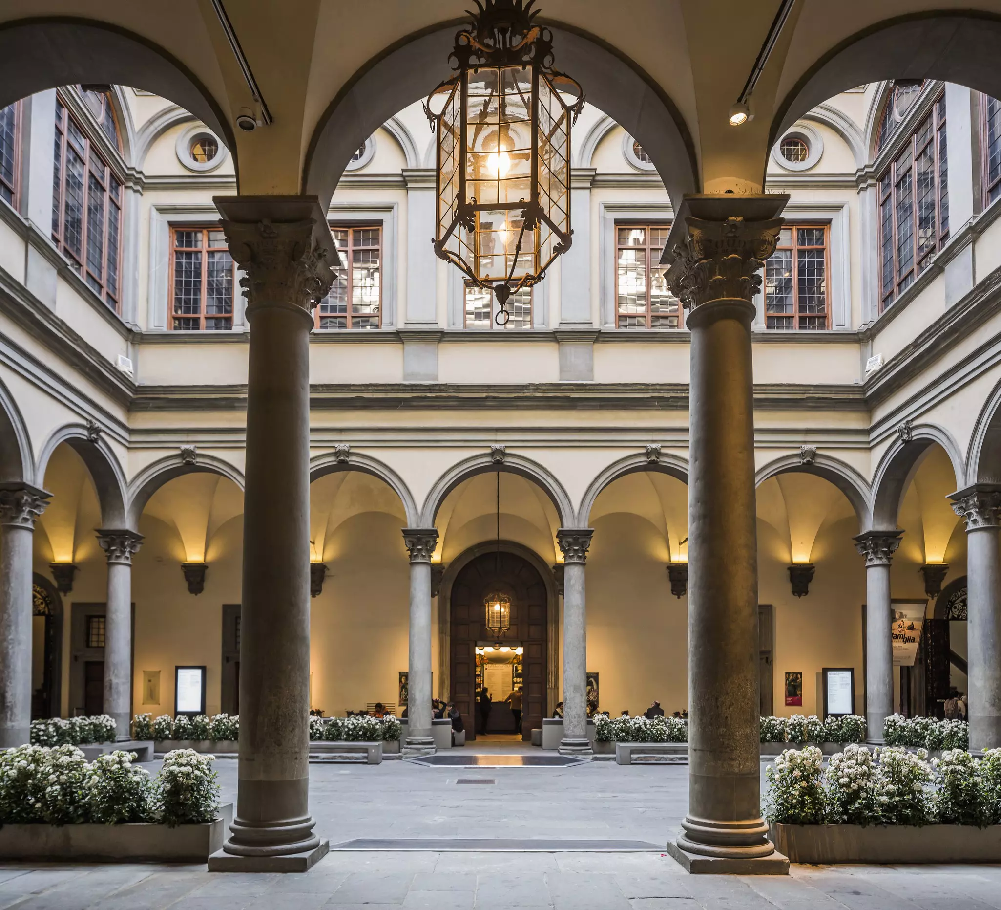 The courtyard of Palazzo Strozzi, warmly lit and lined with white flowers.