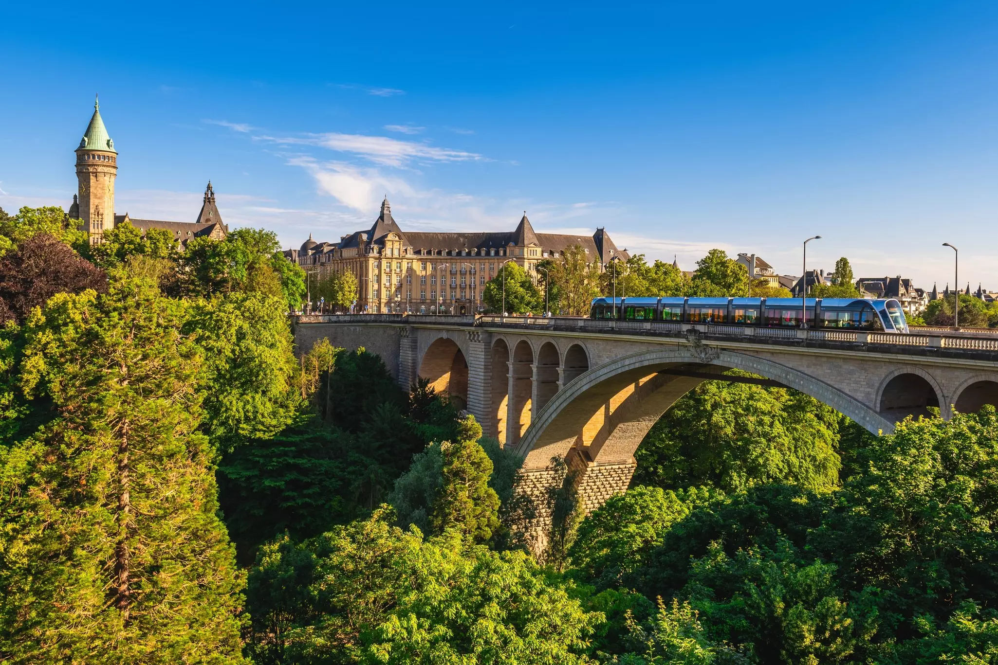 A large stone bridge over a ravine filled with woodland. A tram crosses the bridge.