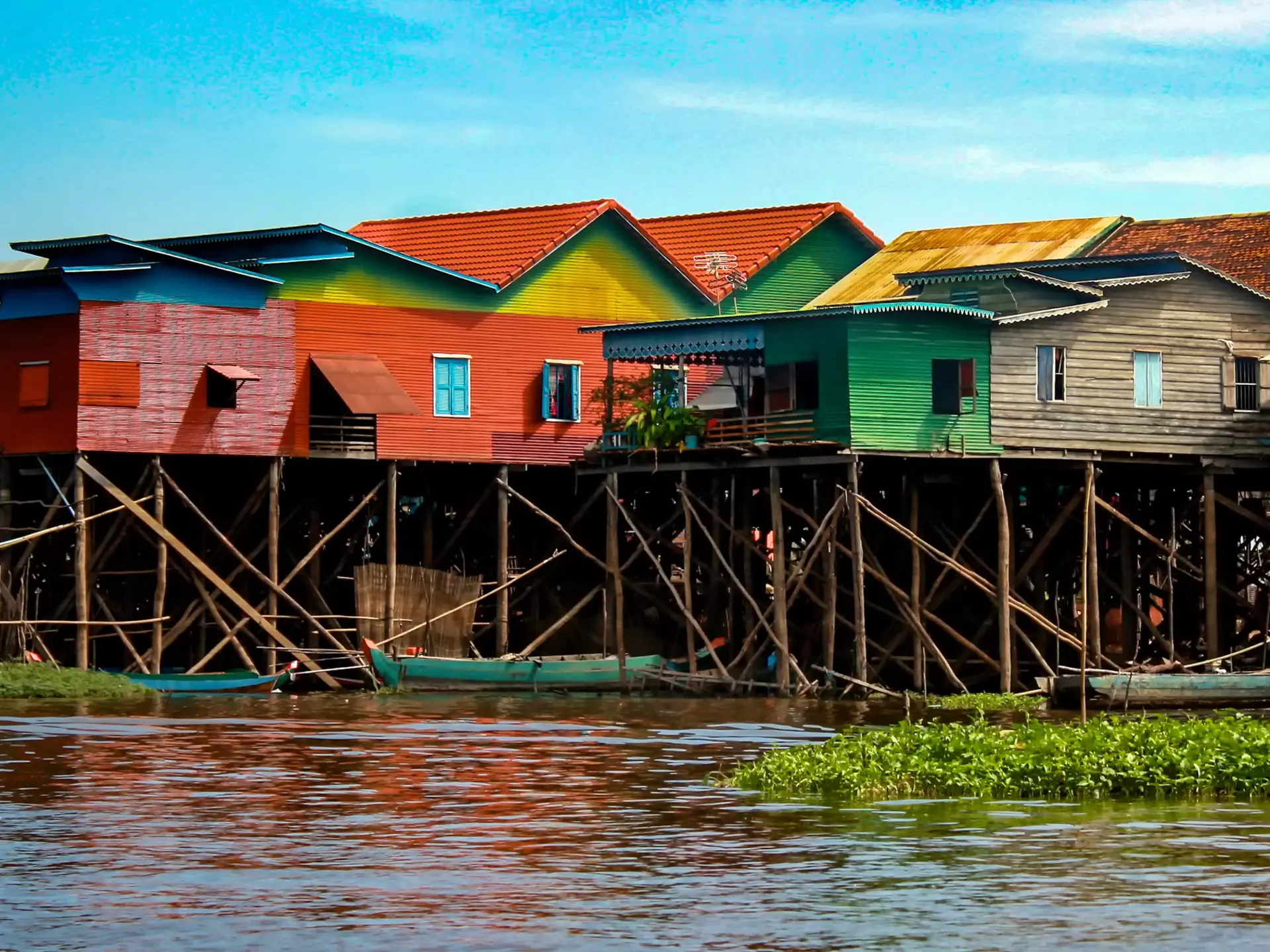 Colorful stilt houses standing above a river with small boats docked under them.