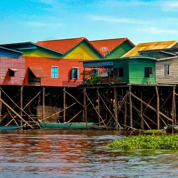 Colorful stilt houses standing above a river with small boats docked under them.