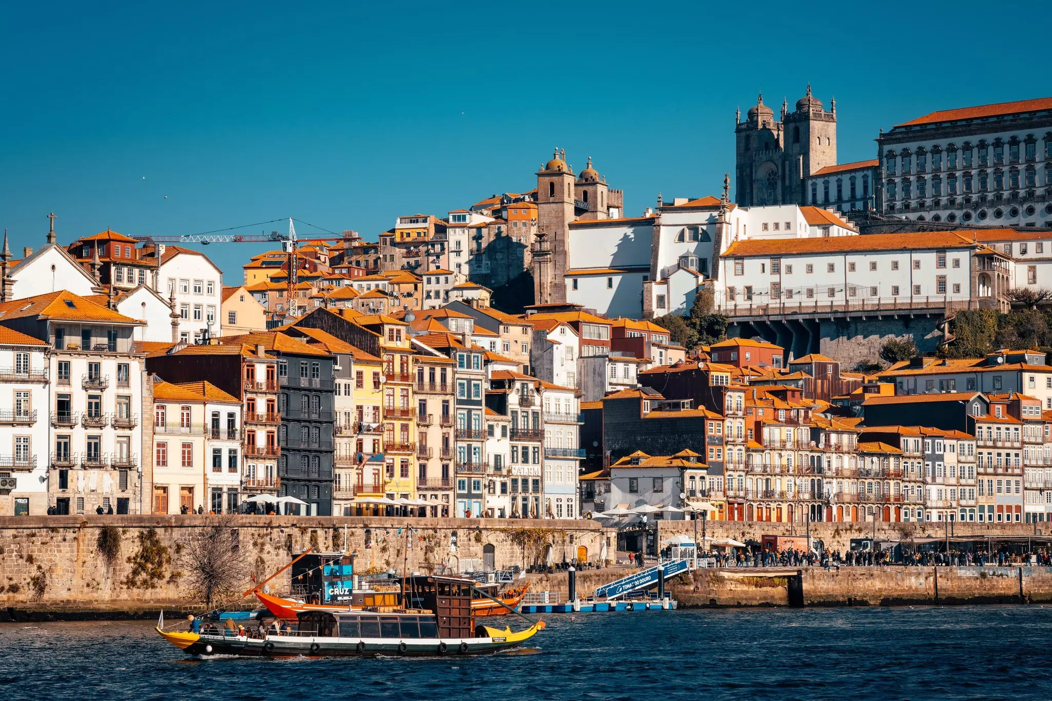 Cityscape with river and boats and a hillside of buildings in the background.