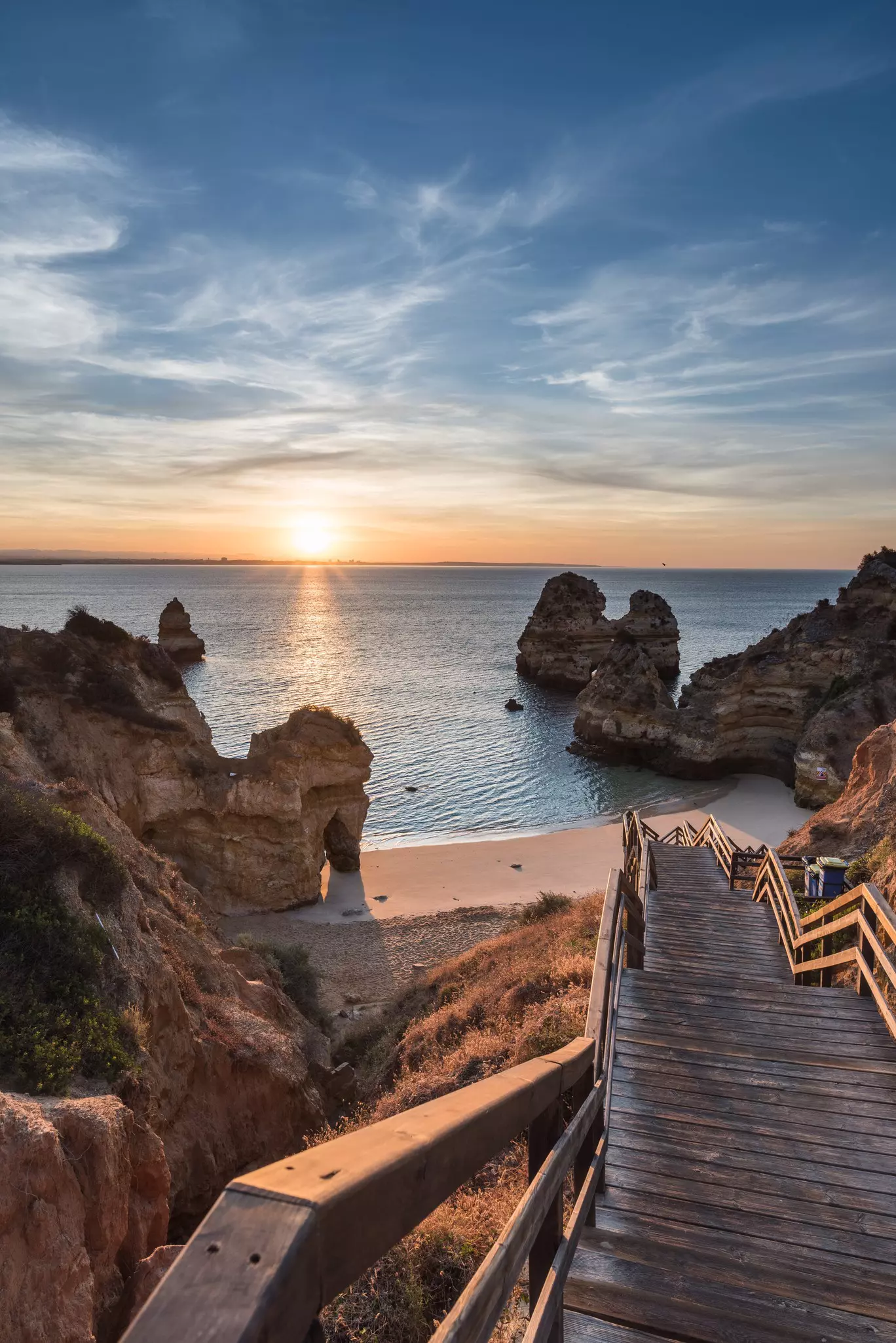 View of wooden steps leading down to Praia do Camilo during sunrise in Lagos, Portugal.