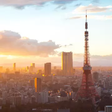 Red and white Tokyo Tower beside dark temple roofs at sunset, with city towers glowing in golden light under clouds.