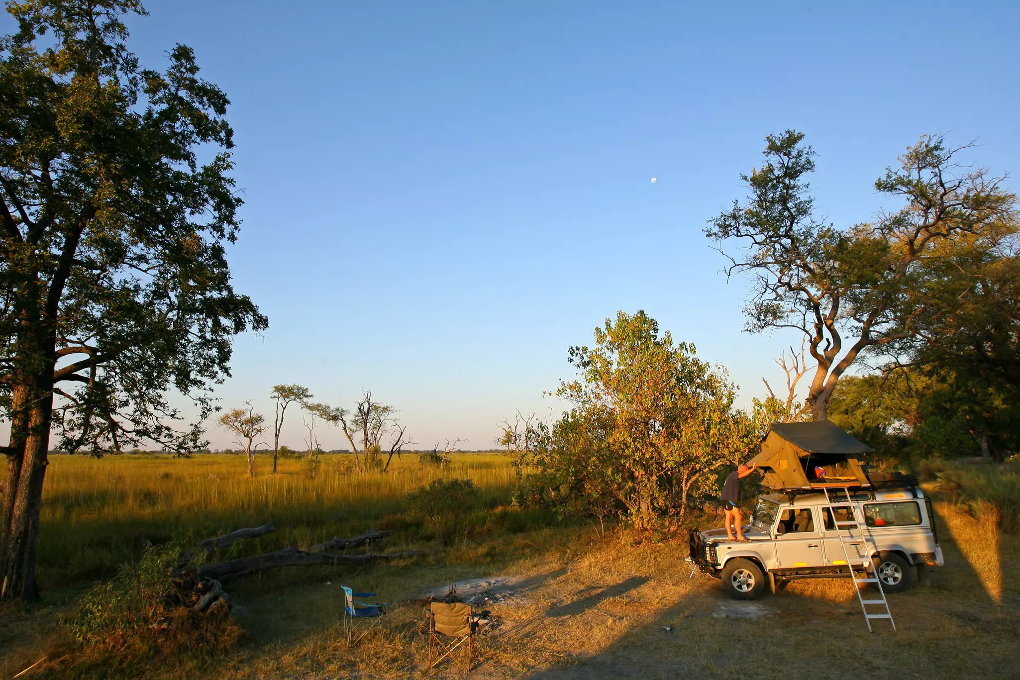 A person setting up a tent on the roof of a 4WD in a Bostwana game reserve
