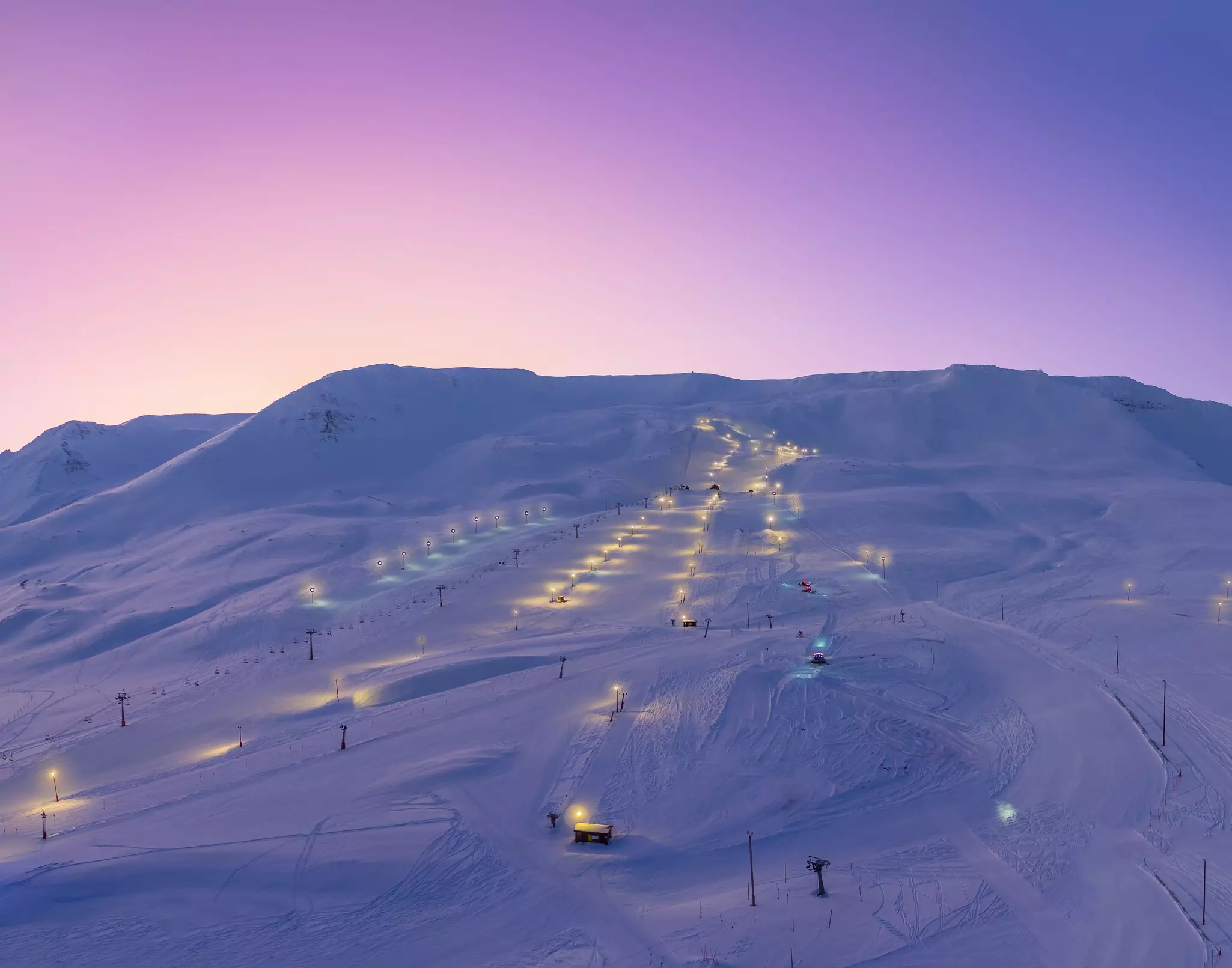 Ski slopes at dusk with lights bordering trails.