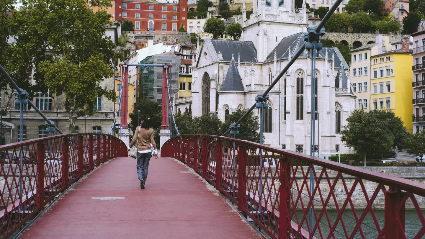 A woman walking on a red footbridge over the Saône river in Lyon
