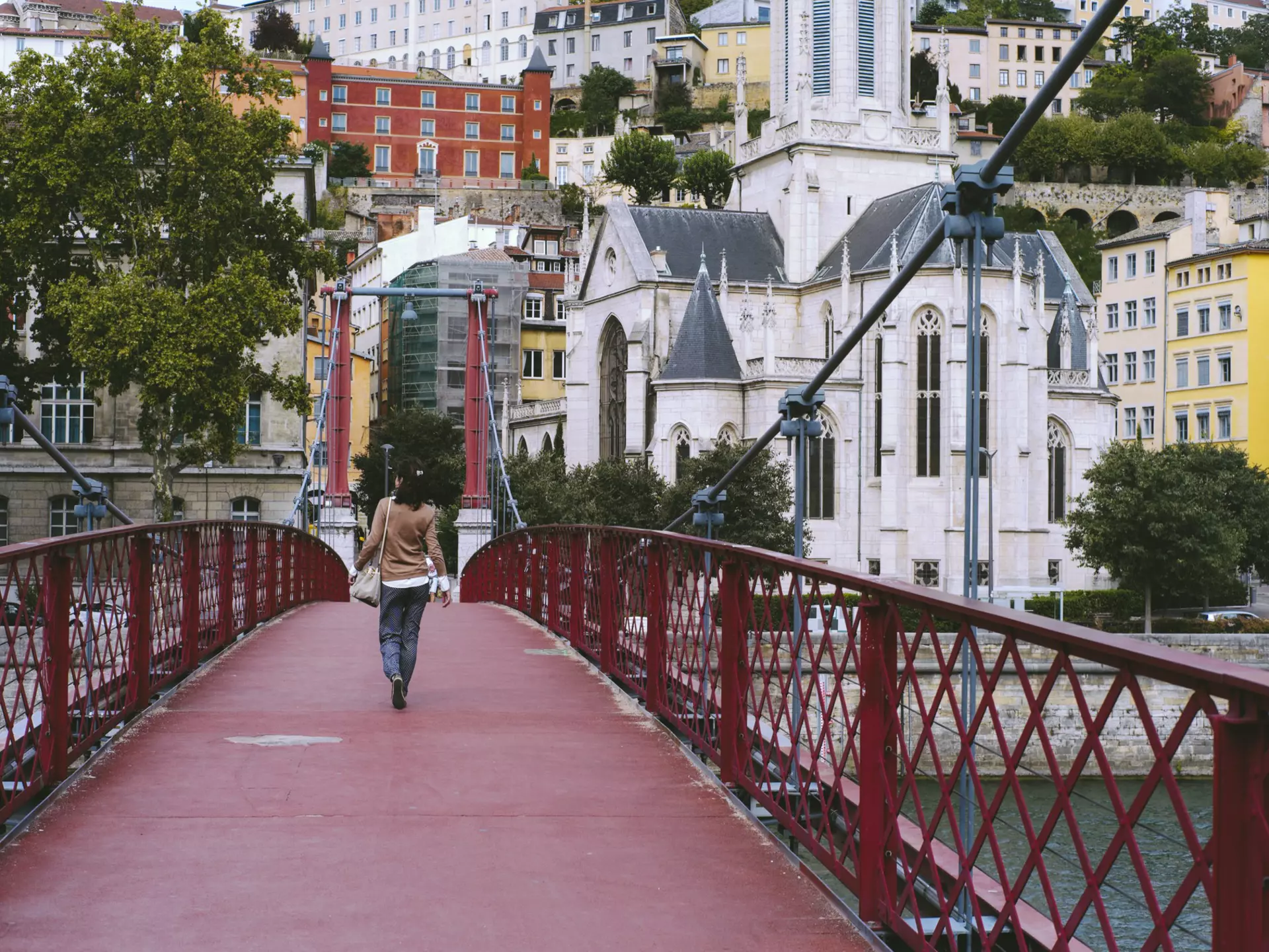A woman walking on a red footbridge over the Saône river in Lyon