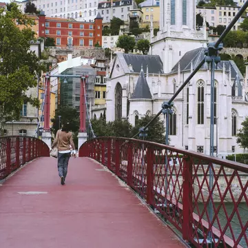 A woman walking on a red footbridge over the Saône river in Lyon