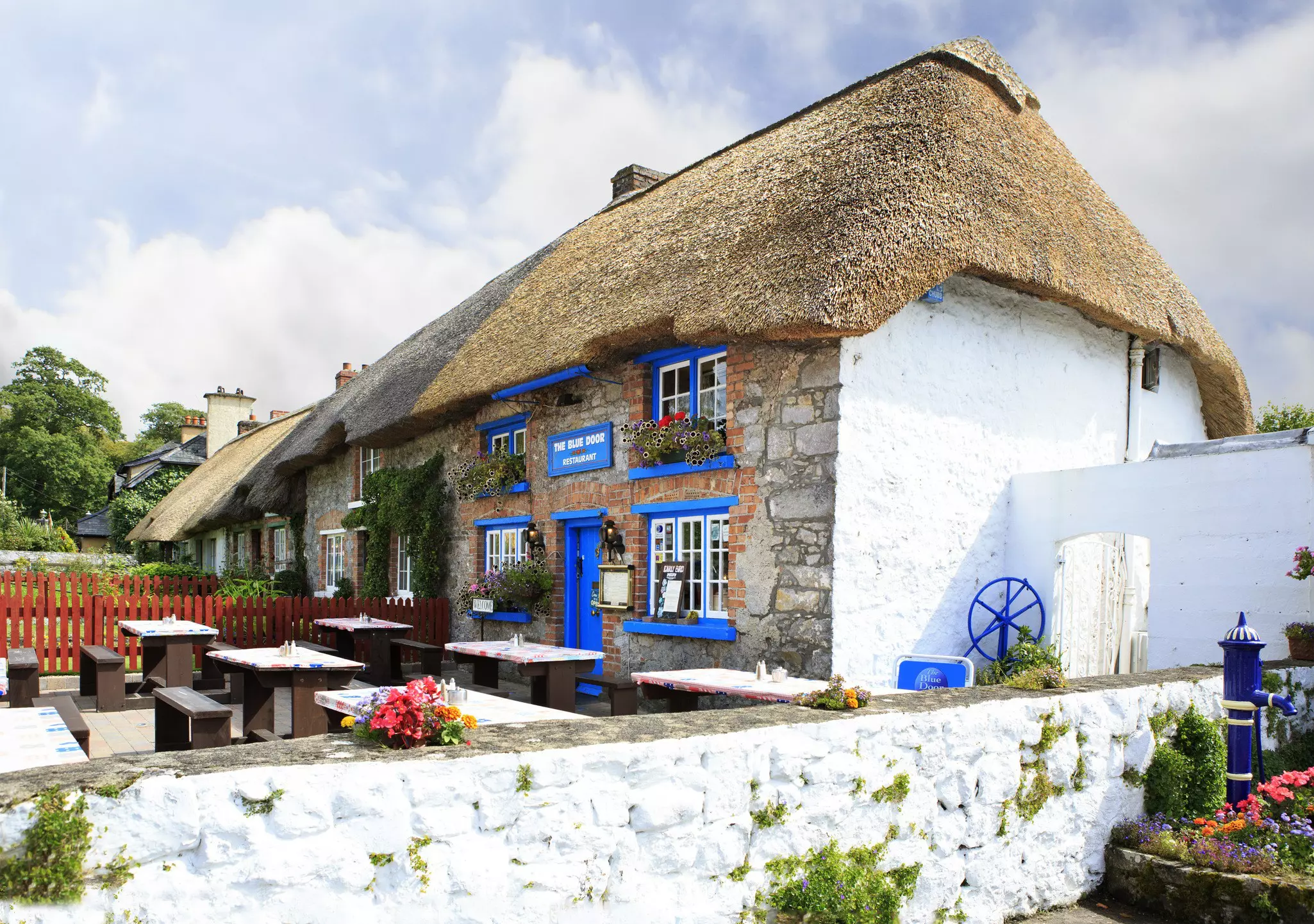 A thatched cottage repurposed as a restaurant. The window- and door-frames are painted blue.