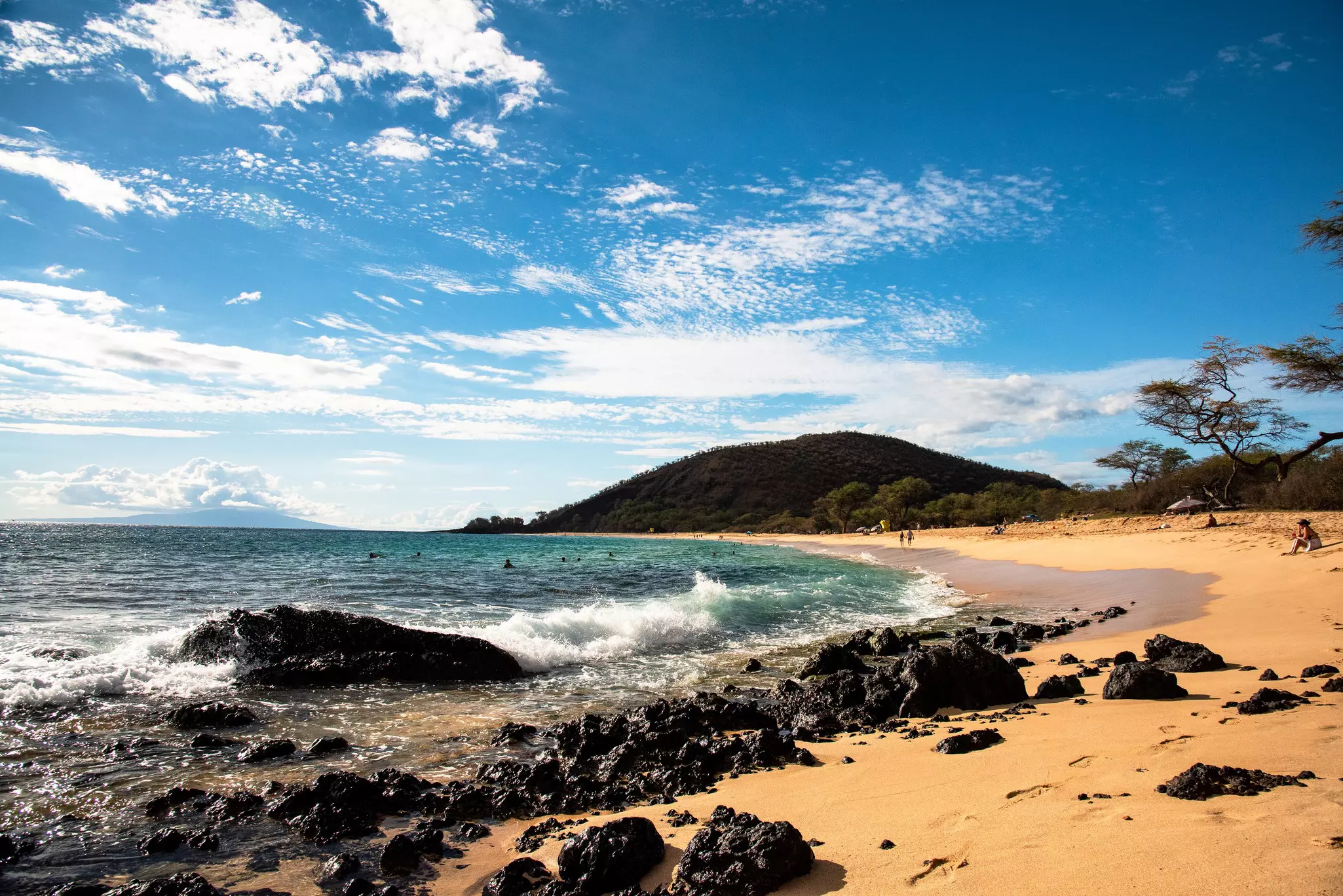 People walking along a large golden arc of sand crashed by waves.