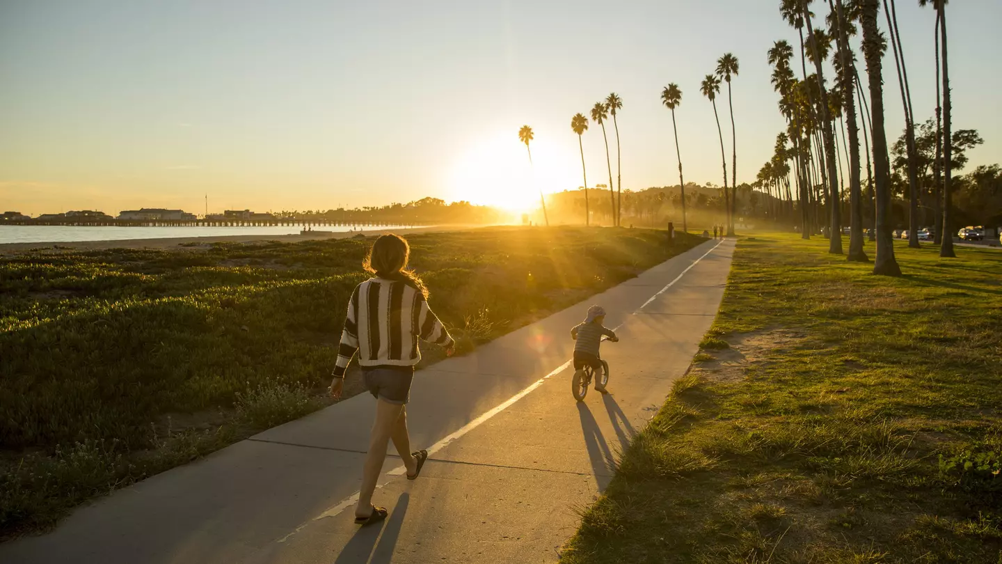 A mother and her son riding a bike along a palm-fringed beachside path in Santa Barbara