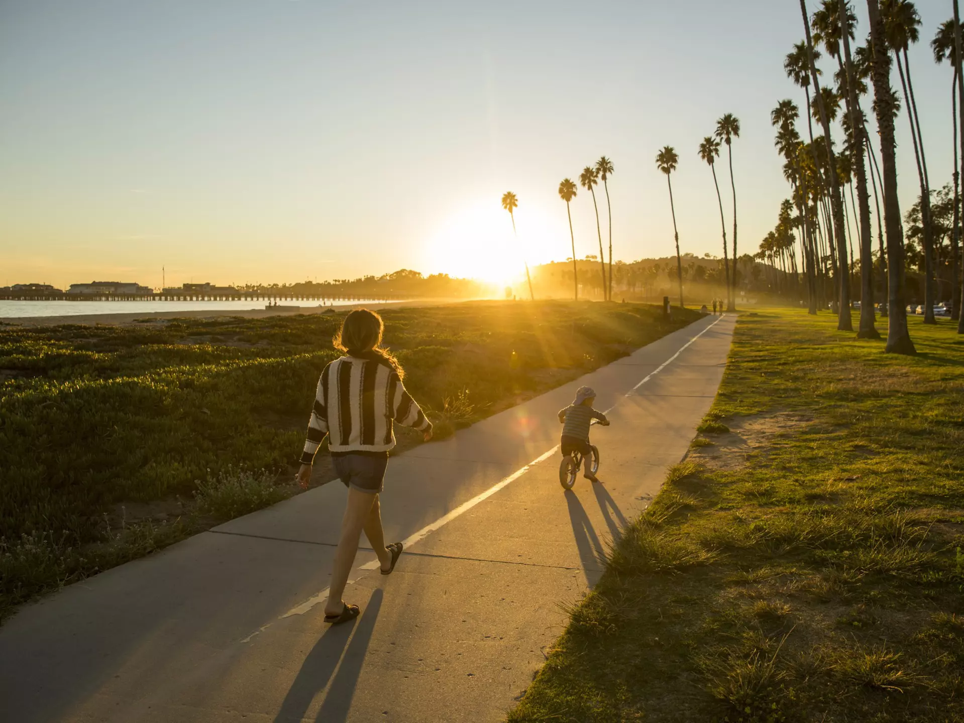 A mother and her son riding a bike along a palm-fringed beachside path in Santa Barbara