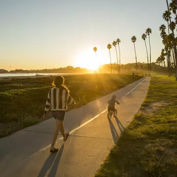 A mother and her son riding a bike along a palm-fringed beachside path in Santa Barbara