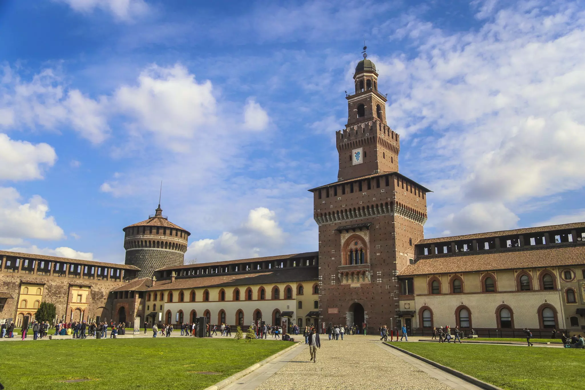 The grounds of a large castle courtyard with tourists strolling the paths.