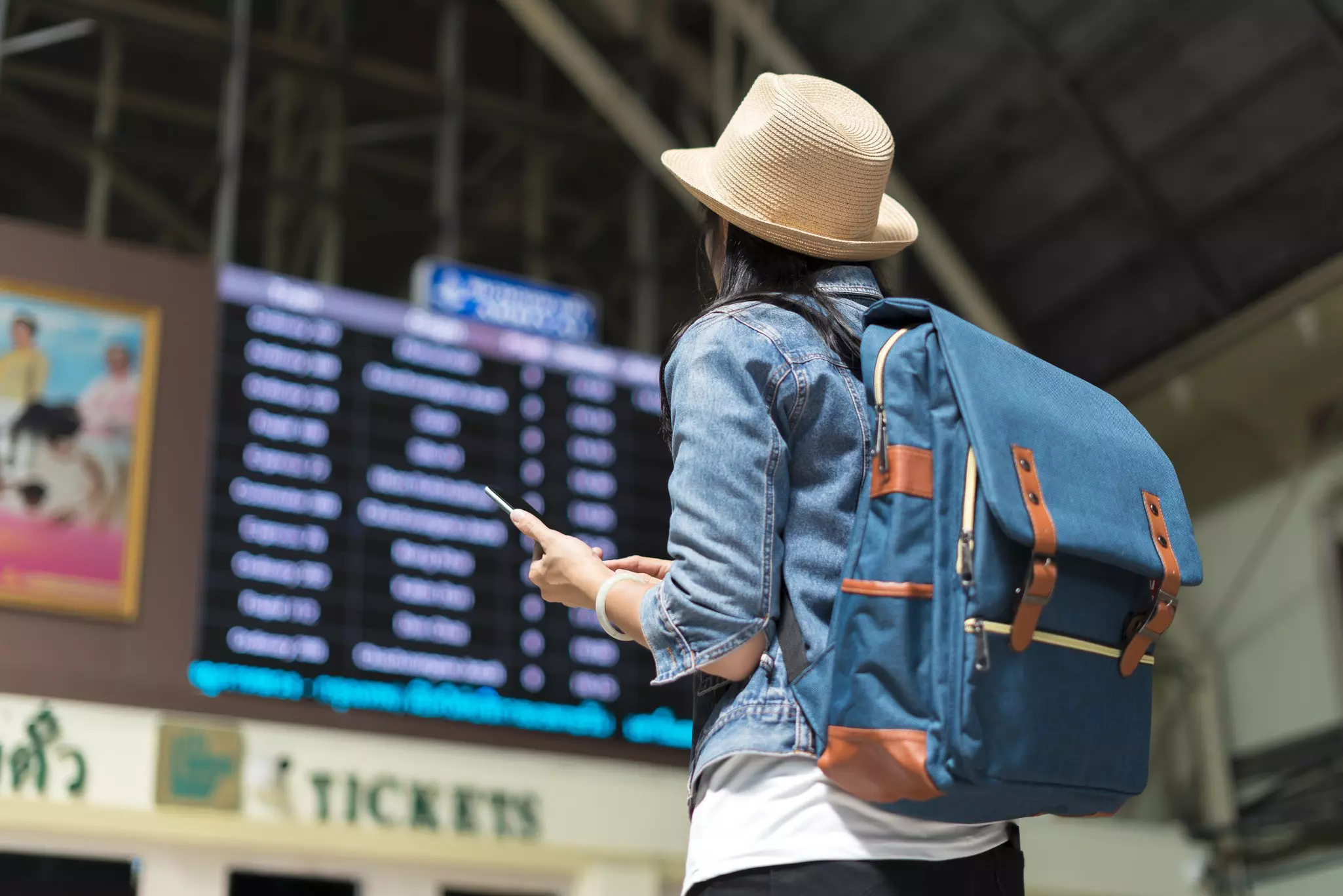 Young female backpacker checking her train arrival on a digital timetable board.