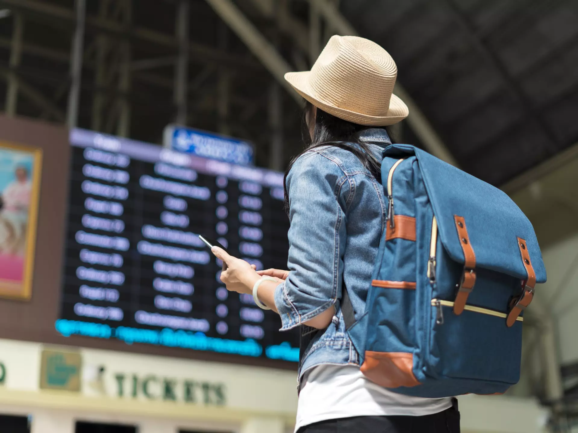 Young female backpacker checking her train arrival on a digital timetable board.