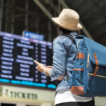 Young female backpacker checking her train arrival on a digital timetable board.